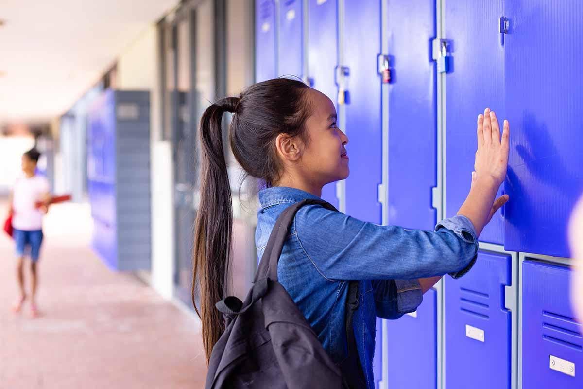 Middle school student opening a blue school locker in a school hallway