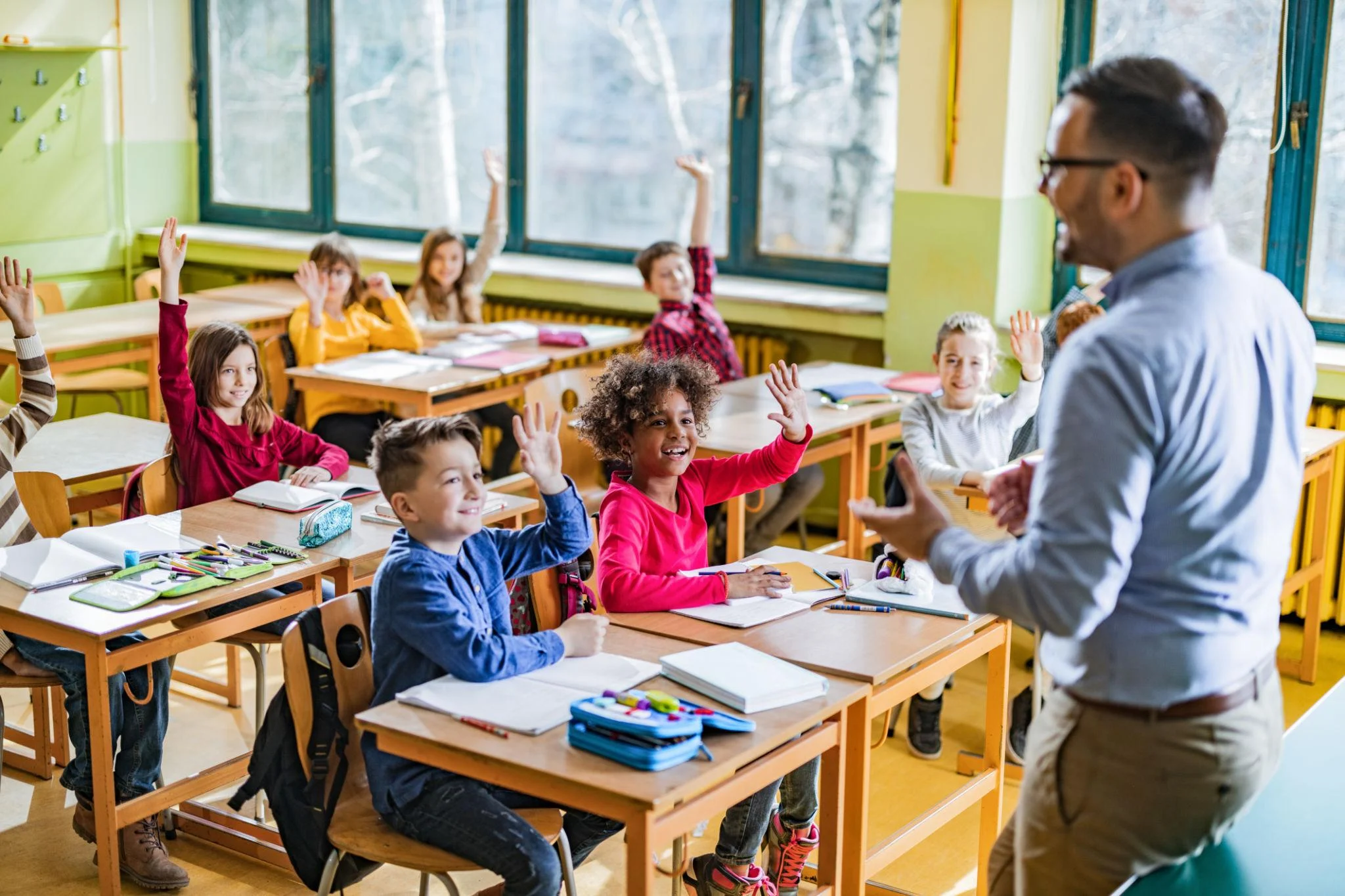Student raising a hand in class during a lesson with other children and a teacher
